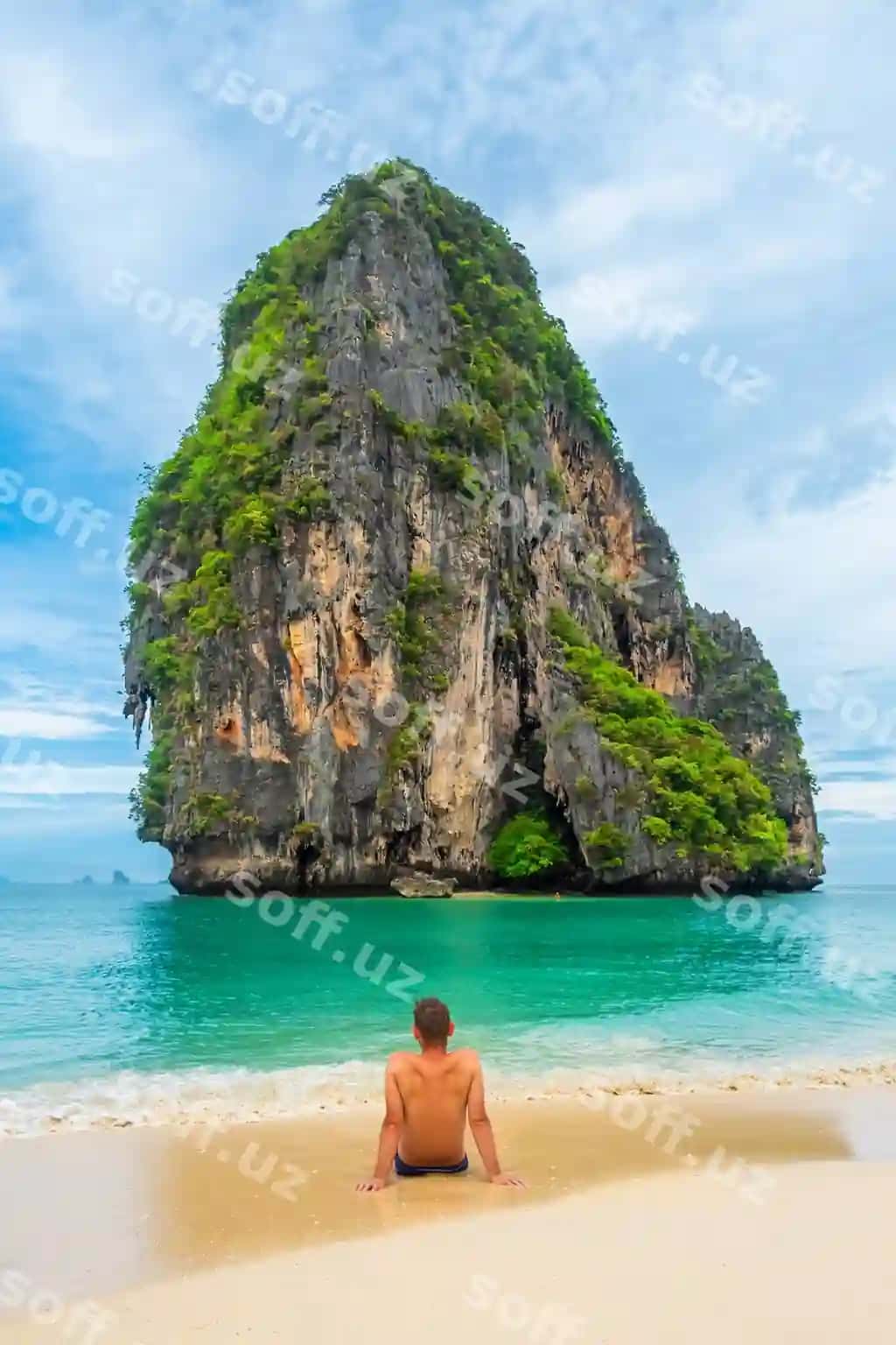 Sayyoh Phra Nang qumli poyintaqasida o'tirgan, Railay Bay Krabidagi qora nok toshli orolni qaraydi. | Man tourist sits phra nang sandy beach looking ko rang nok rocky island railay bay krabi 2