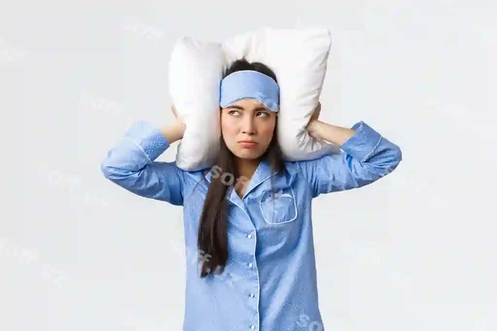 Achinchi, aqlli va haroratli sharqiy qiz insomniyali, pajamalarda yotgan, uyqu maskasi, ko'nganini pillo bilan qoplashgan, talabalik ifodasi, do'stinga qarshi chiqgan, kecha kechasi baland saryog'li, oq fonda. | Annoyed mad grumpy asian girl with insomnia lying bed pajamas sleeping mask cover ears with pillow look bothered irritated with friend snoring loud night white background