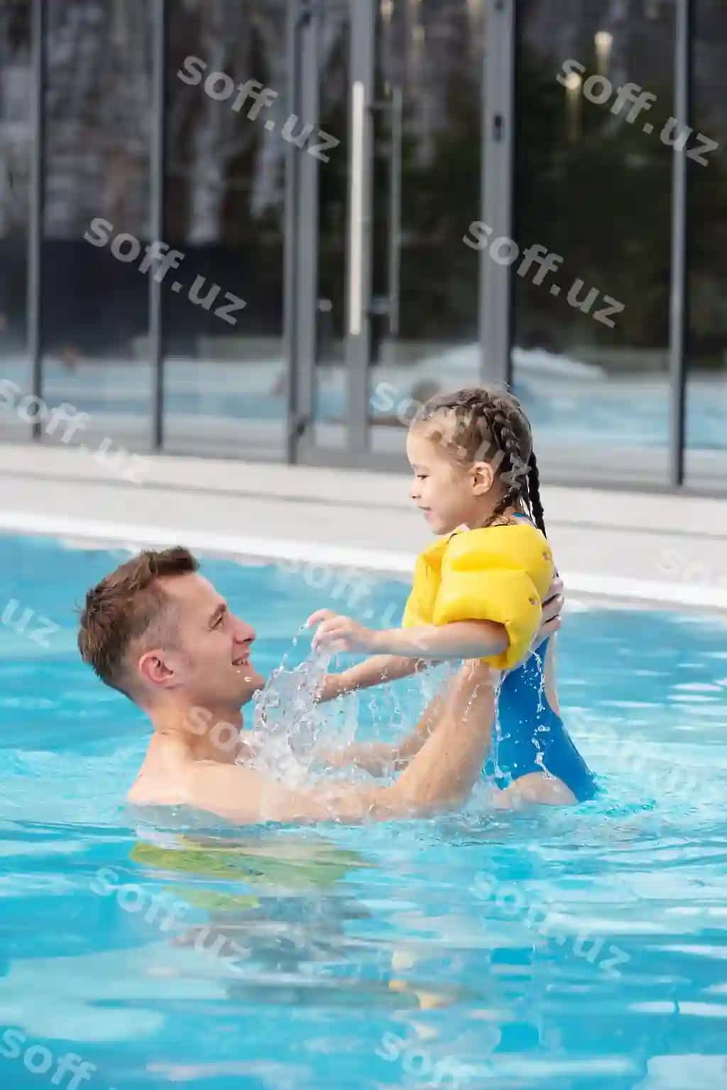 Baxtli yosh erkak o'zining yuqori kichik yoqimli qizini ko'tarayotgan, birgalikda ko'rsatish davomida zamonaviy sport dam olish markazidagi hovuzda. | Happy young man lifting his cute little daughter while having fun together swimming pool contemporary sports leisure center