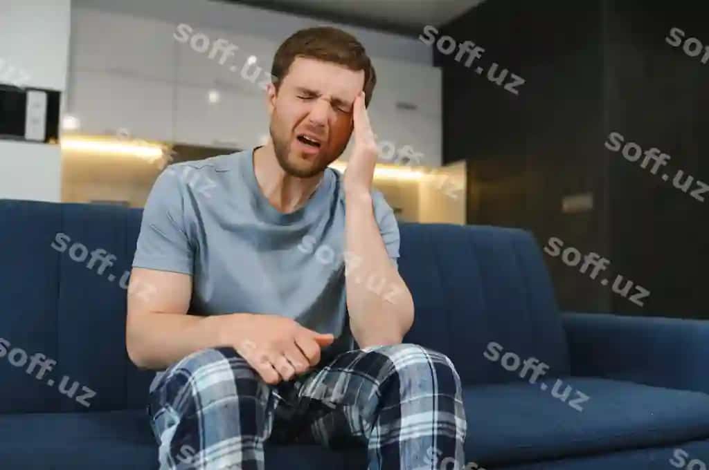 Noaniy og'riq, huzngar, bextsiz chiroyli erkak divan o'rniga o'tirgan, boshini tutgan, bosh og'rigi bilan. | Unpleasant pain sad unhappy handsome man sitting sofa holding his forehead while having headache